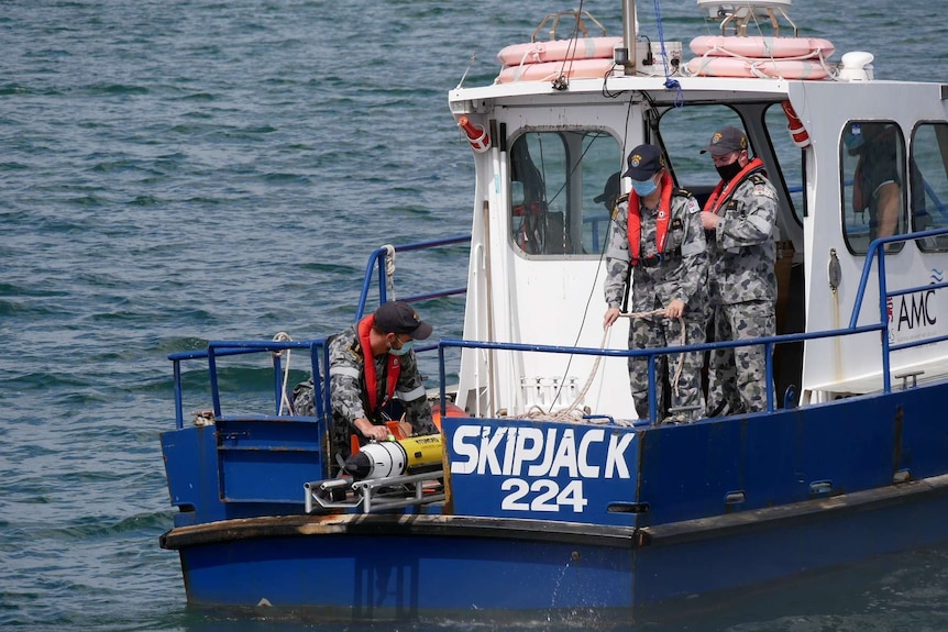 Two Navy personnel bring an AUV on board a boat.