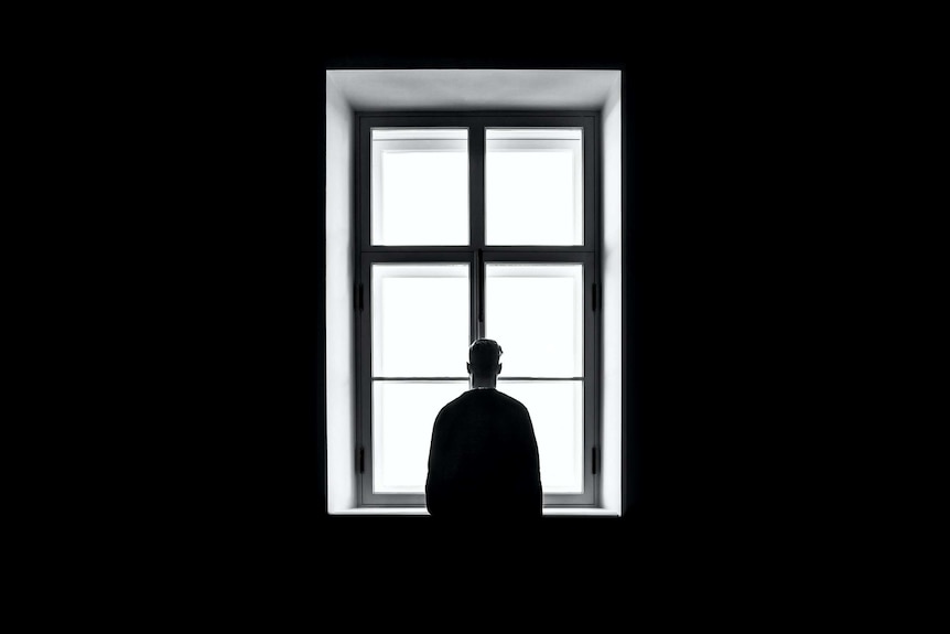 An unidentifiable man stands in front of a large window.