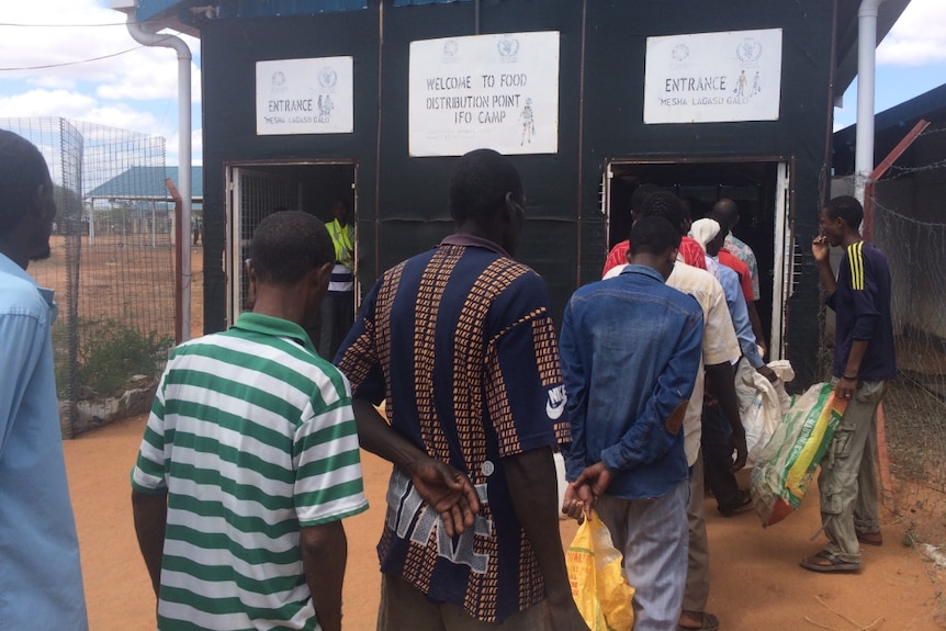 Men line up in front of a hut.