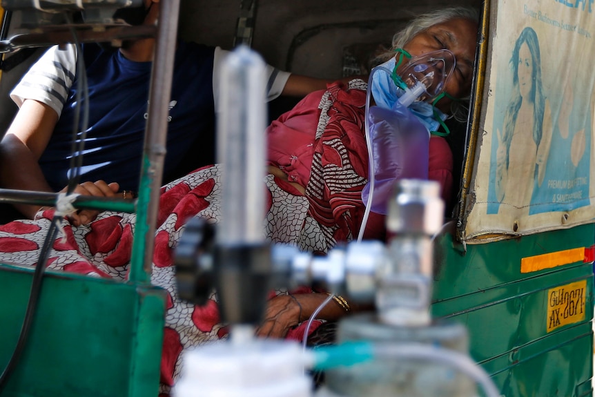 A COVID-19 patient wearing oxygen mask waits inside an auto rickshaw.