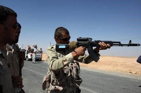 Akram Ramadan, wearing military clothing, looks down the sight of a rifle.