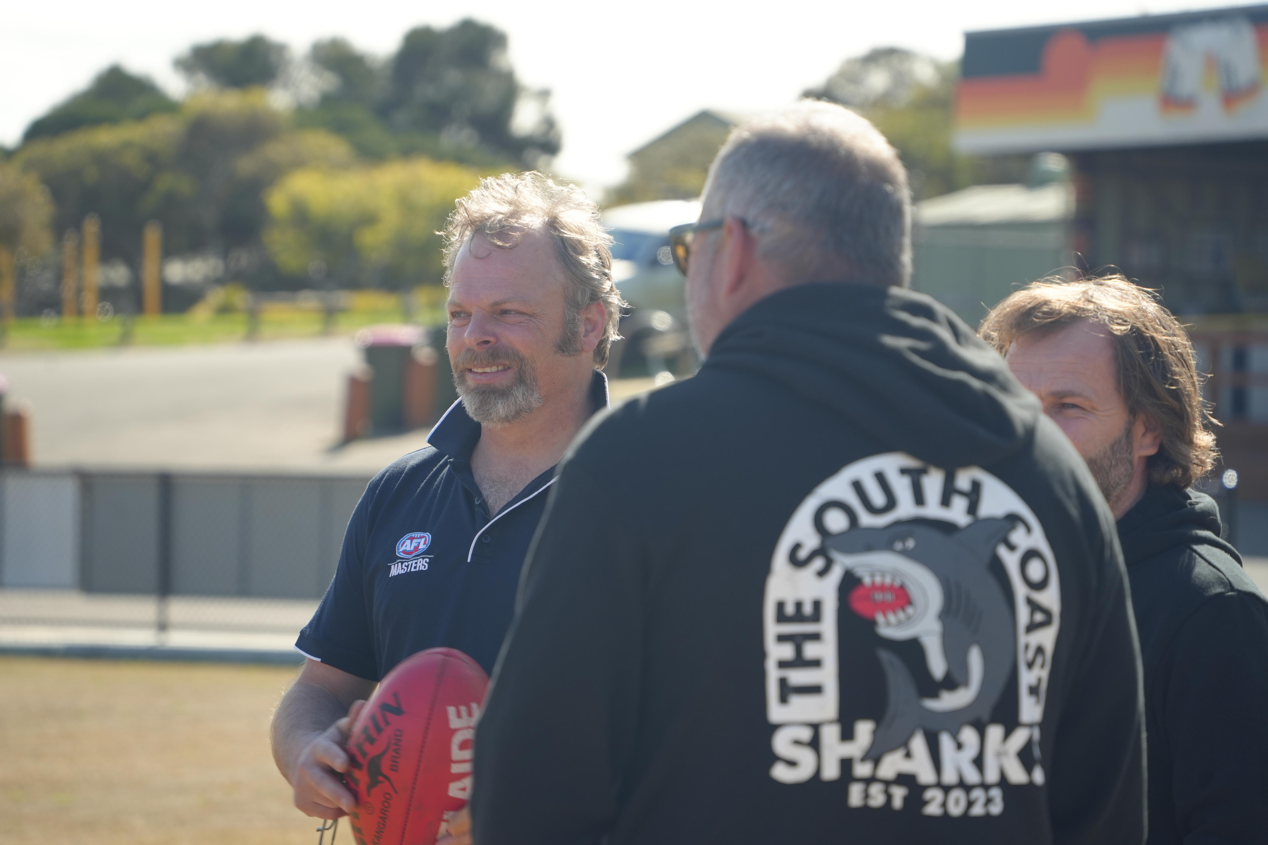 David O'Brien stands in the sun on a football oval chatting to teammates
