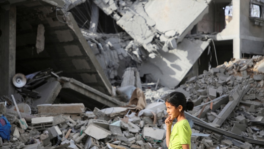 A little girl walks past a house in Rafah destroyed by a missile. It is rubble and debris