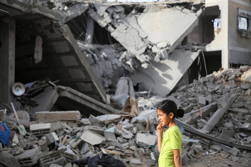 A little girl walks past a house in Rafah destroyed by a missile. It is rubble and debris