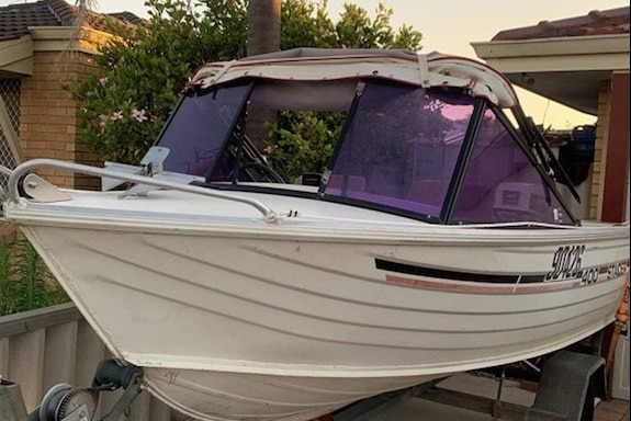 A small boat sits on a trailer on a driveway