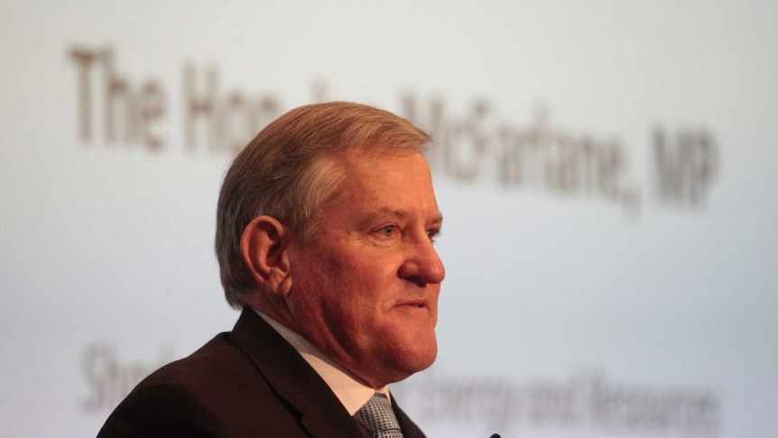 A man stands at a lectern, with a screen behind him that reads the Hon Ian Macfarlane MP