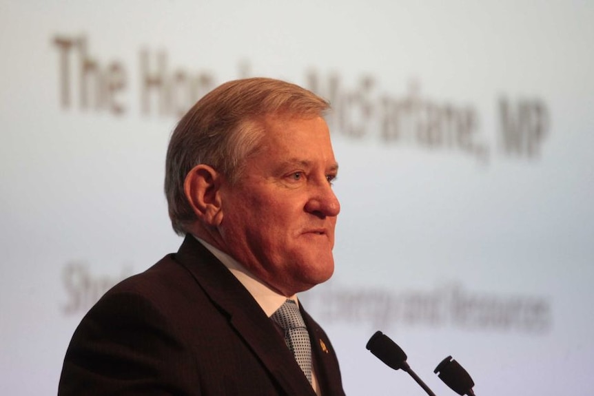 A man stands at a lectern, with a screen behind him that reads the Hon Ian Macfarlane MP