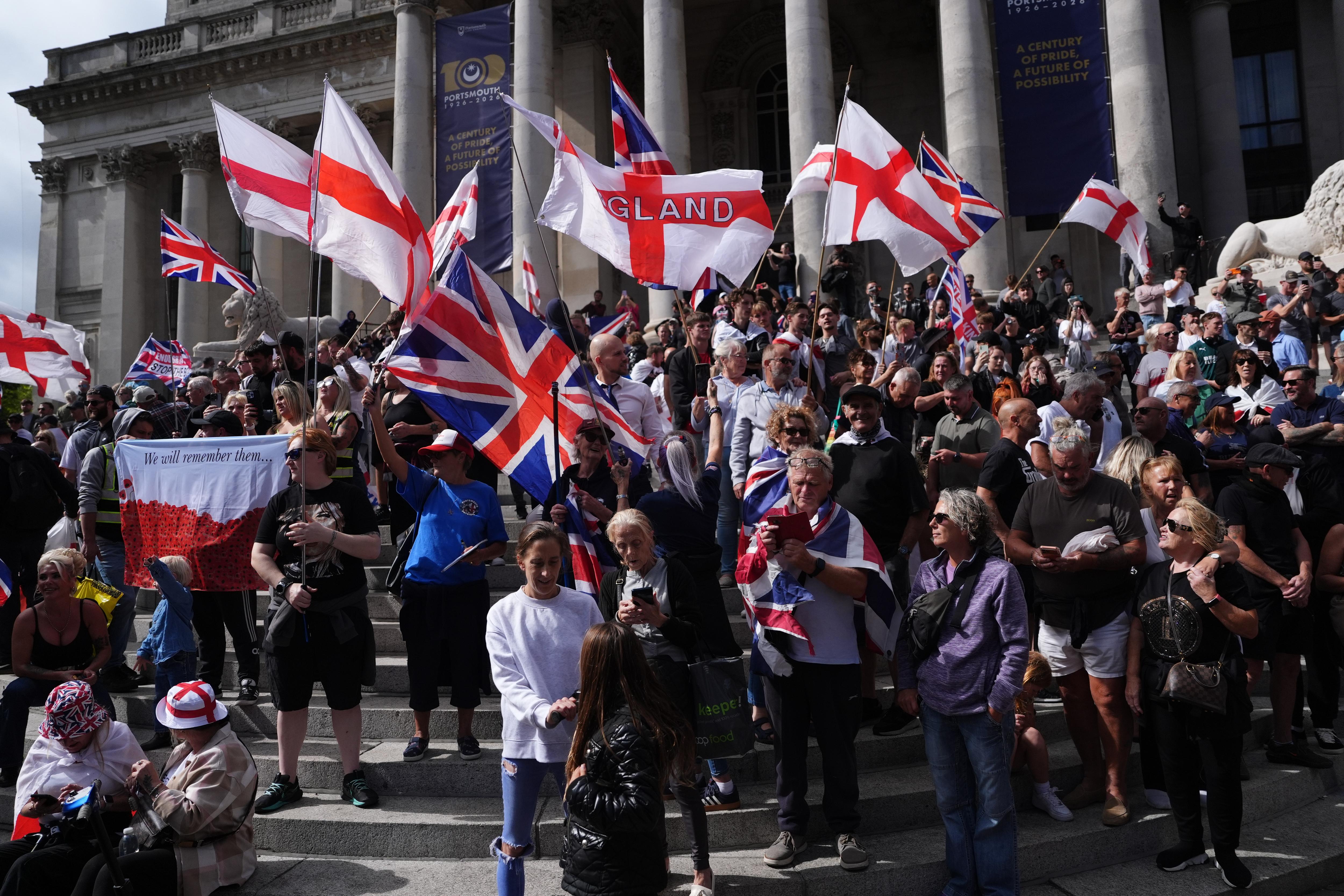 A large protest group carrying English and Union Jack flags on the steps of an ornate building.