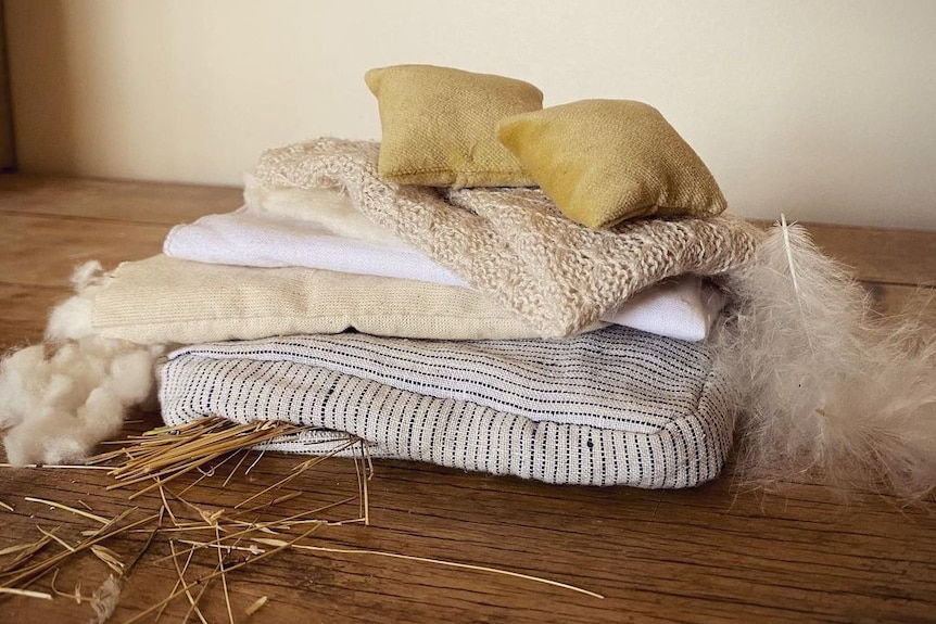 Photograph of a tiny handmade mattress with grass tuffing poking out, and a feather to one side