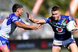 A Warriors NRL player holds the ball with his left hand as he uses his right to attempt to palm a Bulldogs opponent.