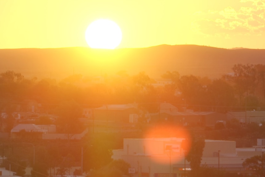 The sun setting over a hill west of Broken Hill with houses in the foreground.