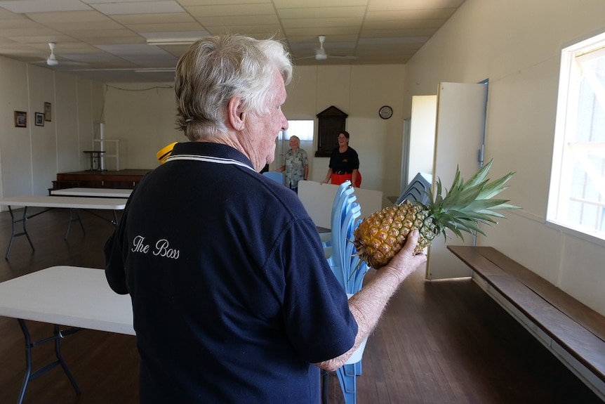 A woman, wearing a tee-shirt that says 'the boss', carries a pineapple at a CWA hall.