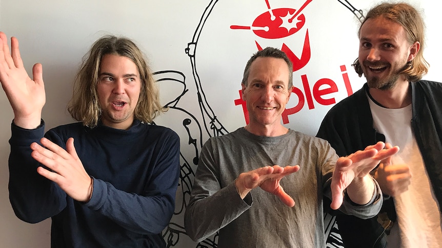 Photograph of Konstantin and Lewis from The Belligerents standing with Richard Kingsmill infront of a triple j logo.