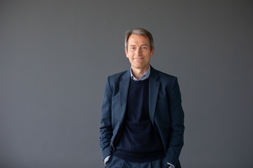 A man in a suit standing in front of a grey wall. 