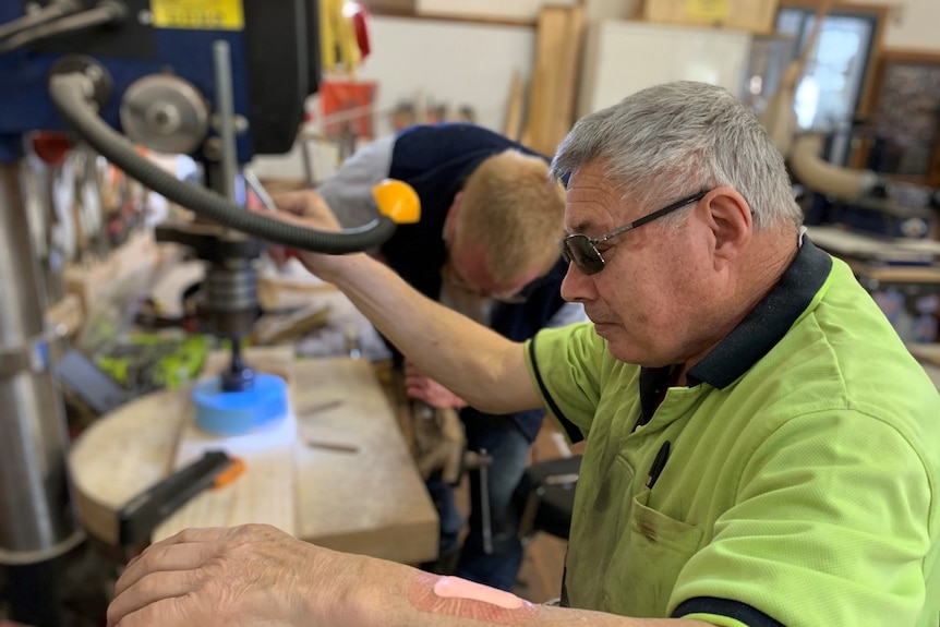 A man with silver hair uses a lathe in a workshop