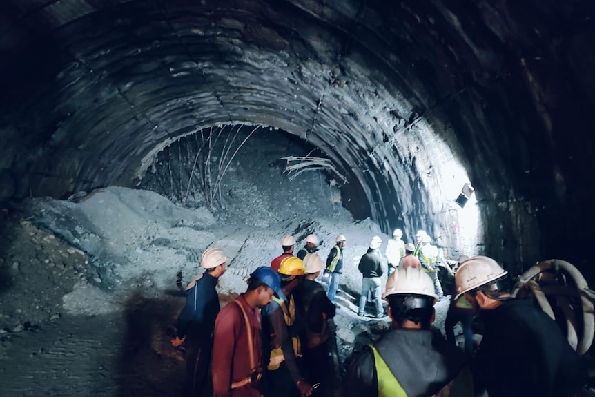 An collapsed tunnel is pictured with workers wearing hardhats standing in front of it.