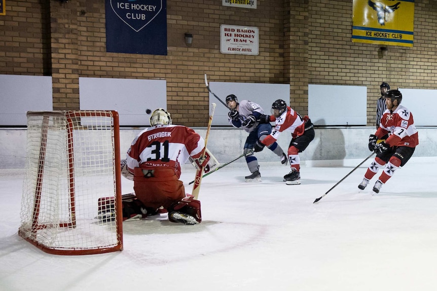 Four ice hockey players and a referee play in front of a goal on an ice rink.