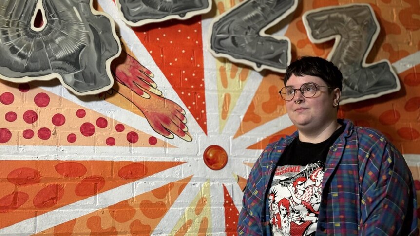 A person standing infront of a red and yellow mural that says 4ZZZ in grey text. 