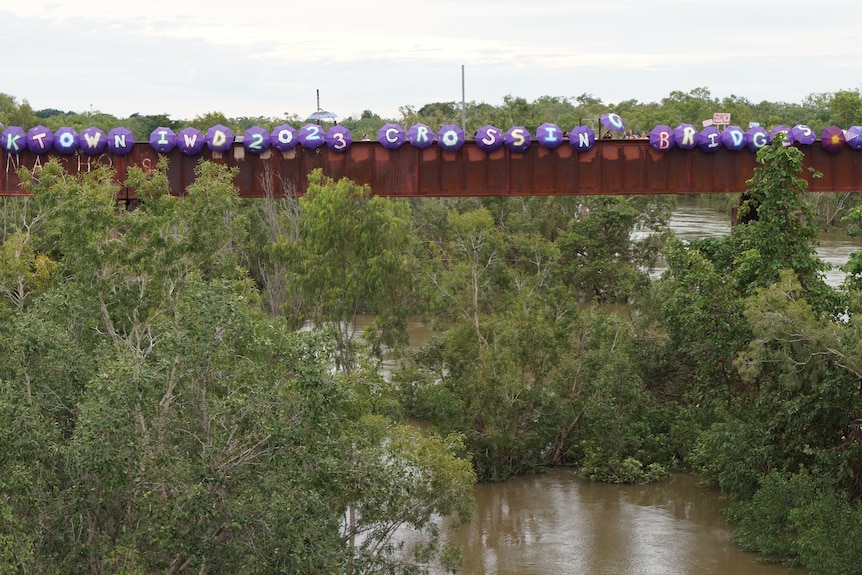 crowds hold purple umbrellas spelling k town iwd 2023 crossing bridges