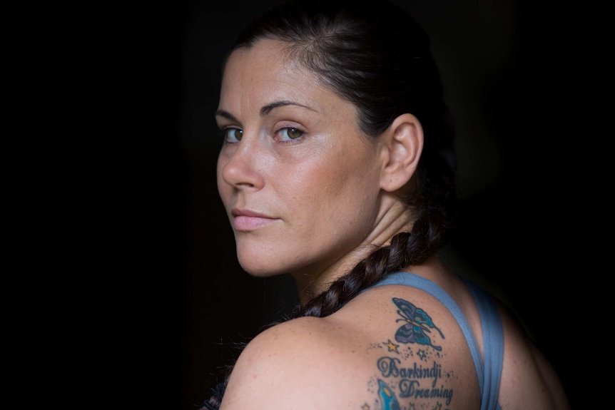 Close-up of a woman looking into the camera, showing a shoulder tattoo.