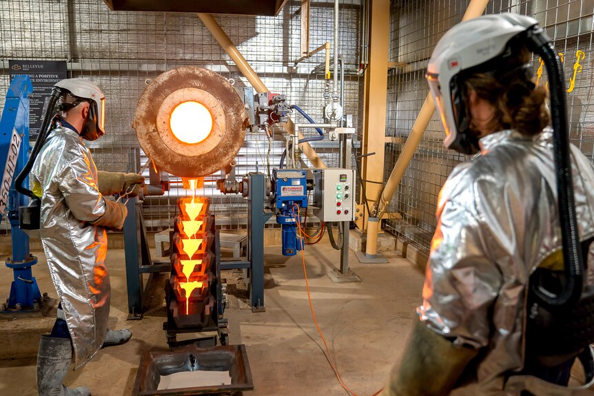 Liquid gold is poured at Bellevue gold mine, as two people wearing protective silver suits watch over.
