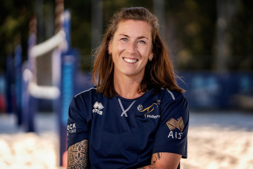 National beach volleyball coach Margo Wiltens smiles as she stands on a beach vollyball court