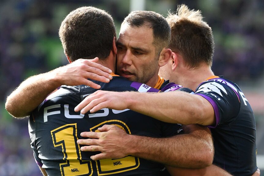 Two male NRL players hug as they celebrate a try being scored by their team.