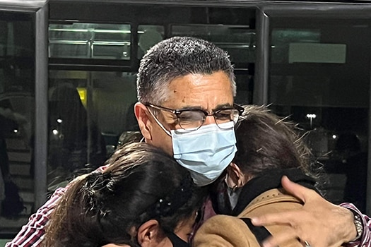Two young women hug an older man. All are wearing face masks.