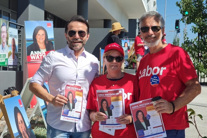 Two men and a woman holding up Labor election materials smile for a photo.