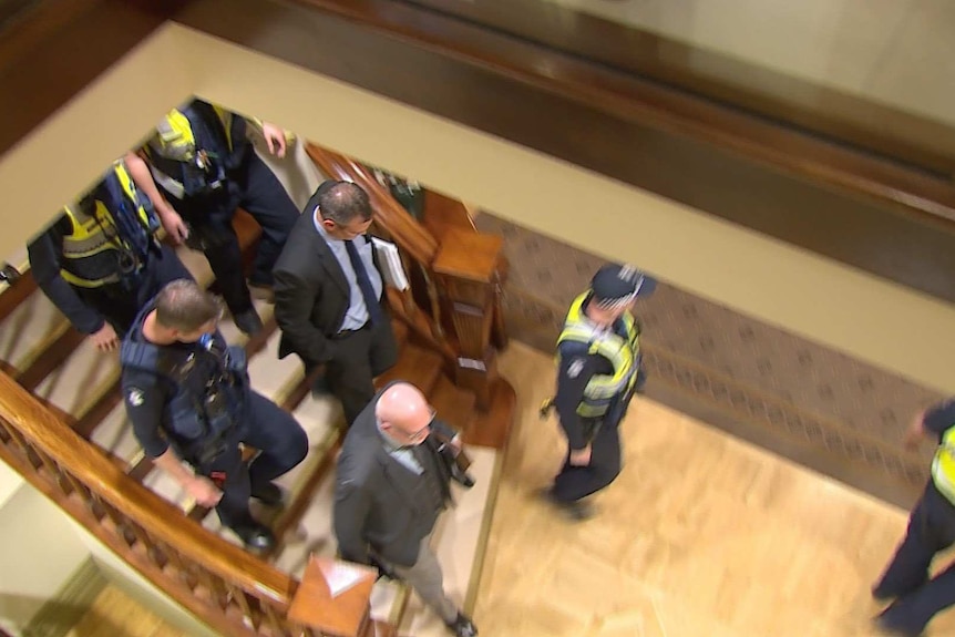 A man is surrounded by police, walking down stairs.