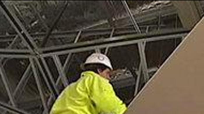 Two construction workers putting up a ceiling in an apartment building.