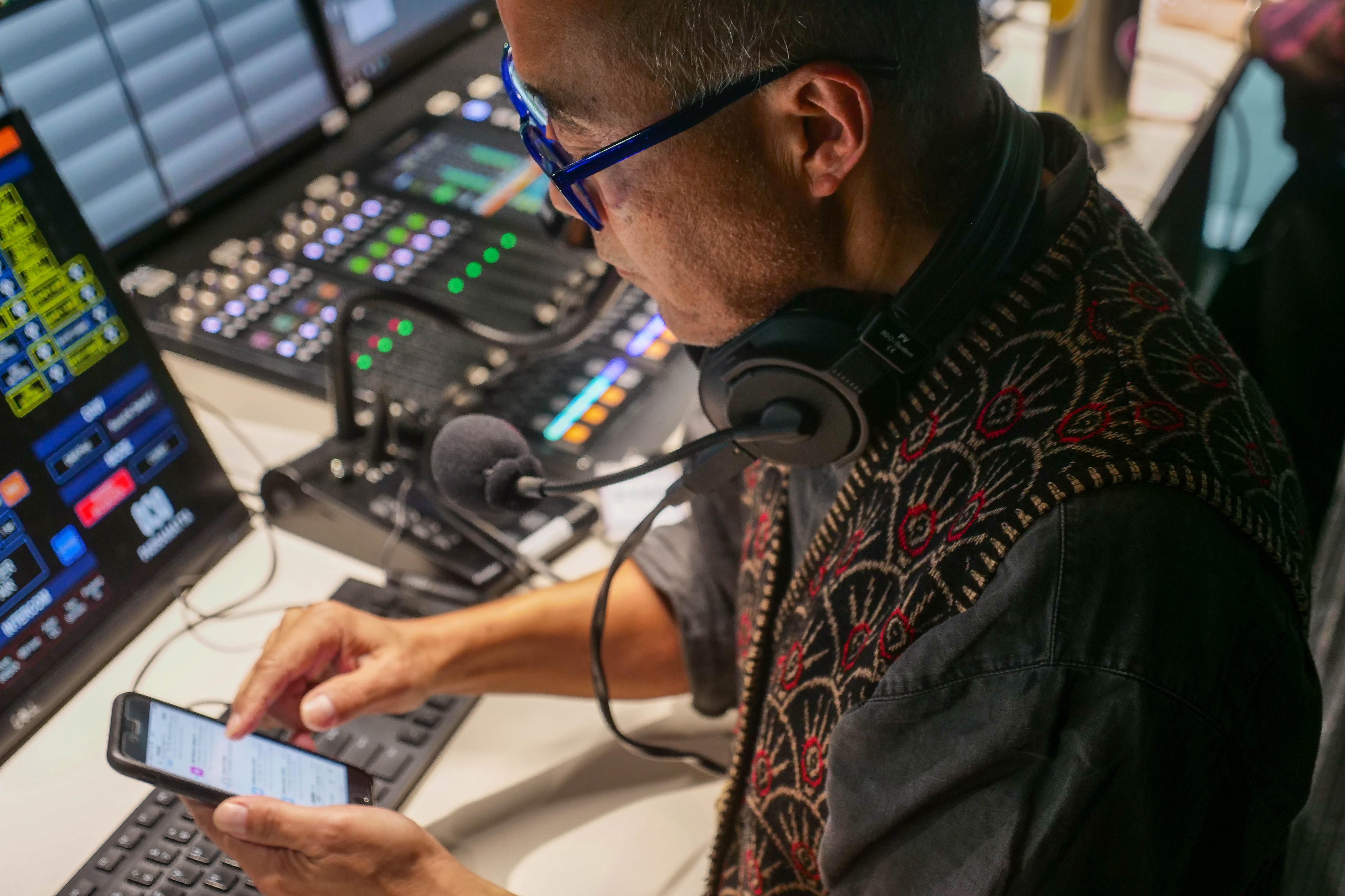 a man looks at his mobile phone while standing at a radio production desk