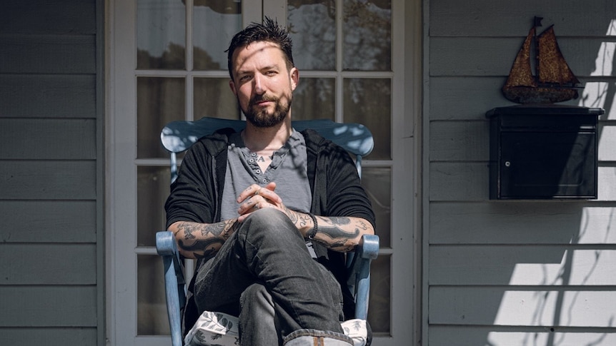 Frank Turner sits barefoot with legs crossed in a blue chair on a porch