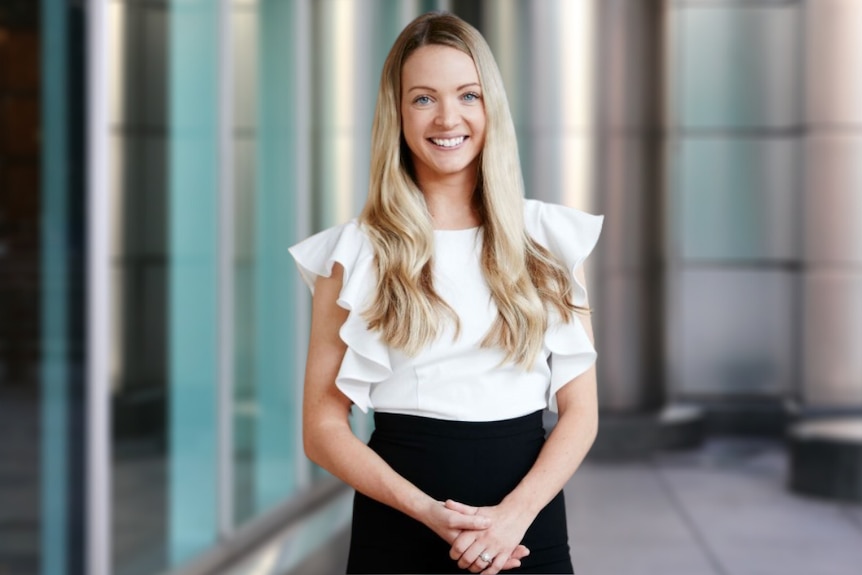 Une femme aux cheveux blonds souriant dans une chemise blanche et une jupe noire