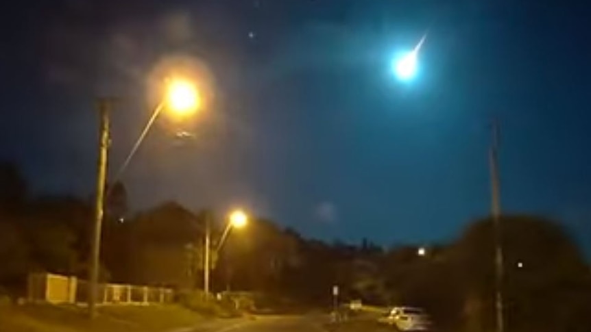 Meteor seen in sky above roadway at night.