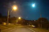 Meteor seen in sky above roadway at night.