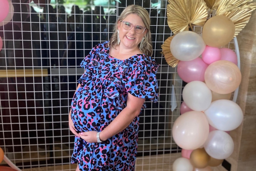 Ash Webb smiling and surrounded by balloons while heavily pregnant