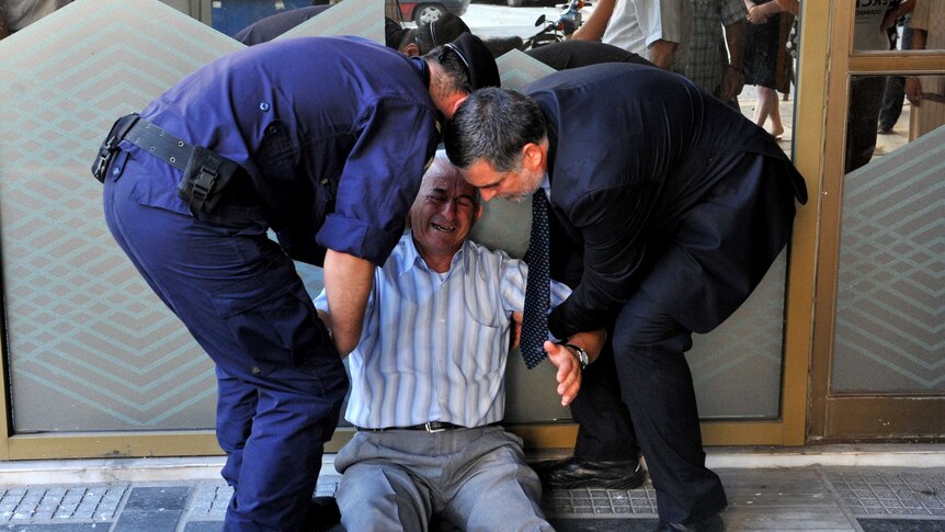 Police assist an elderly man crying outside a Greek bank