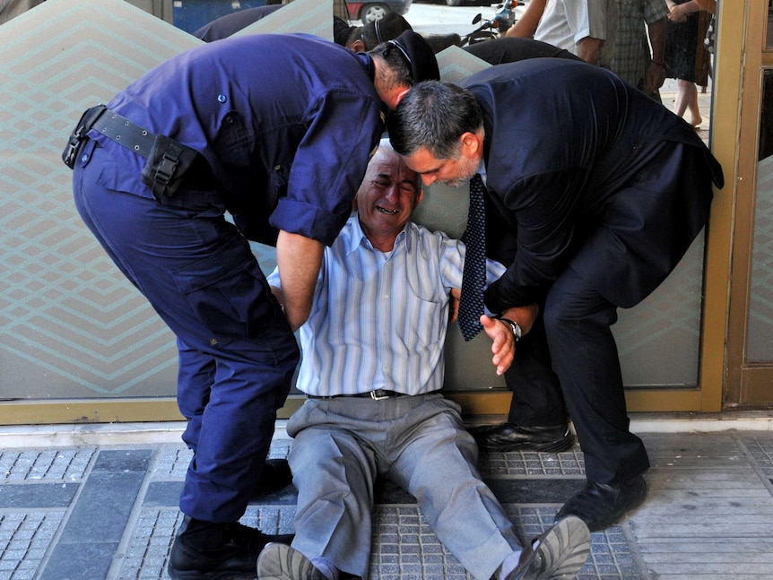 Police assist an elderly man crying outside a Greek bank