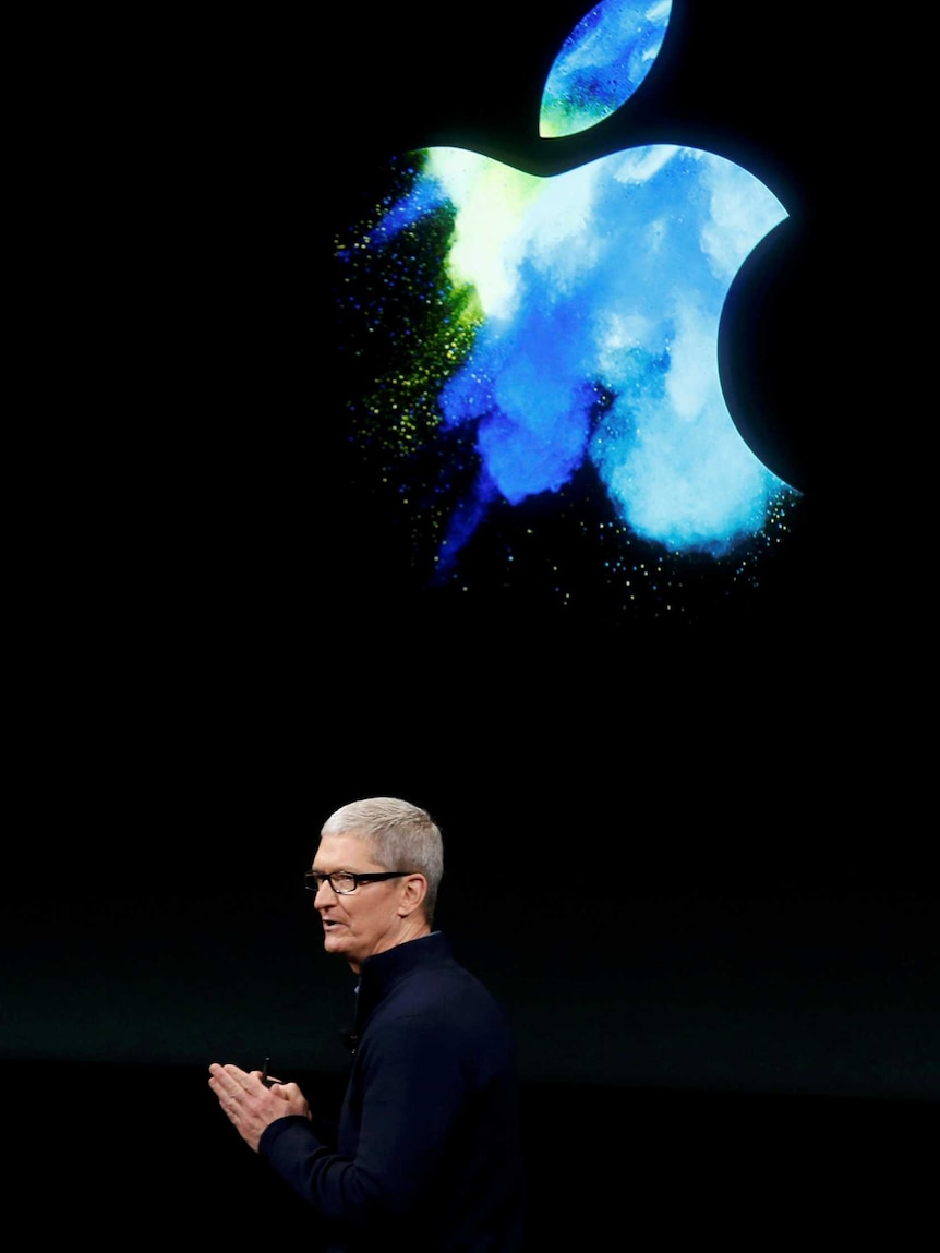 Apple CEO Tim Cook stands under Apple logo.