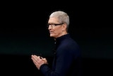 Apple CEO Tim Cook stands under Apple logo.