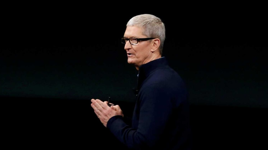 Apple CEO Tim Cook stands under Apple logo.