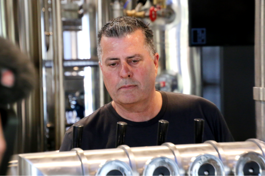 A man with short grey hair stands at a bar in front of beer handles.