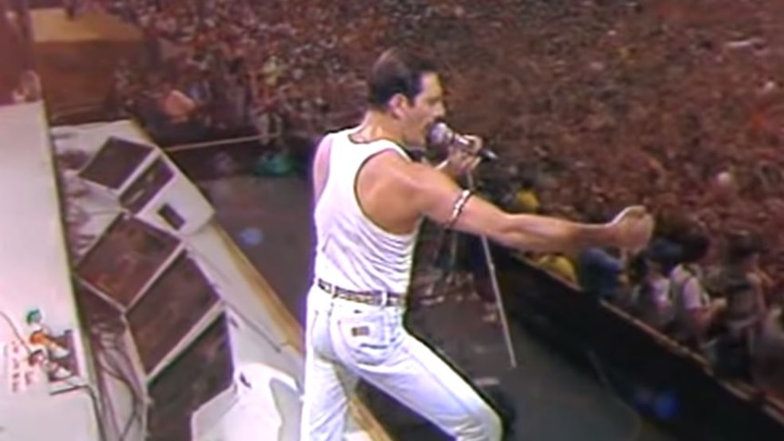 Freddie Mercury holds microphone stand in front of audience