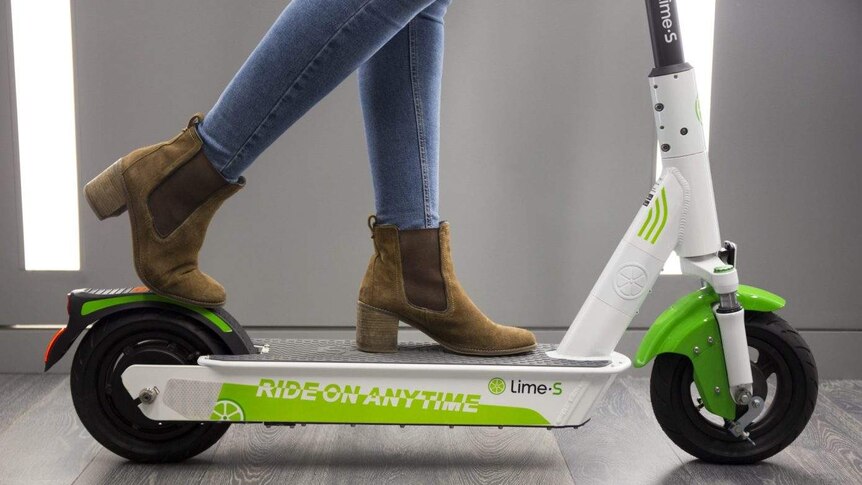 A person from the knees down with a Lime brand electric scooter