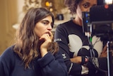 A woman stands next to another woman, she's directing a shoot on a music video set