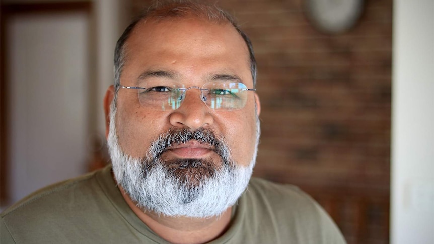 A close up photo of Nav Mittal wearing reading glasses and looking at the camera.