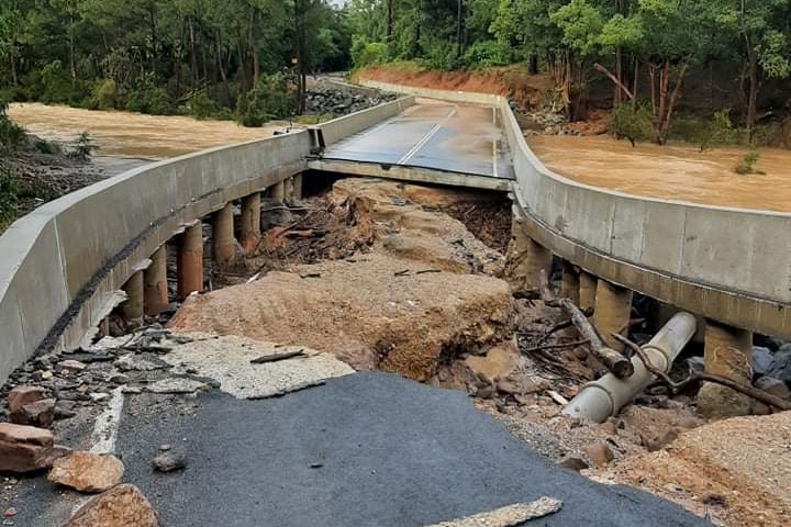 A bridge over a brown river that has been damaged and washed out. 