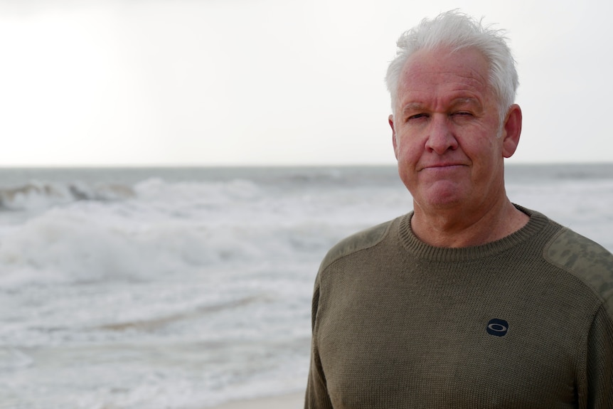 Mitch Thorson stands on the beach with the surf rolling in behind him.