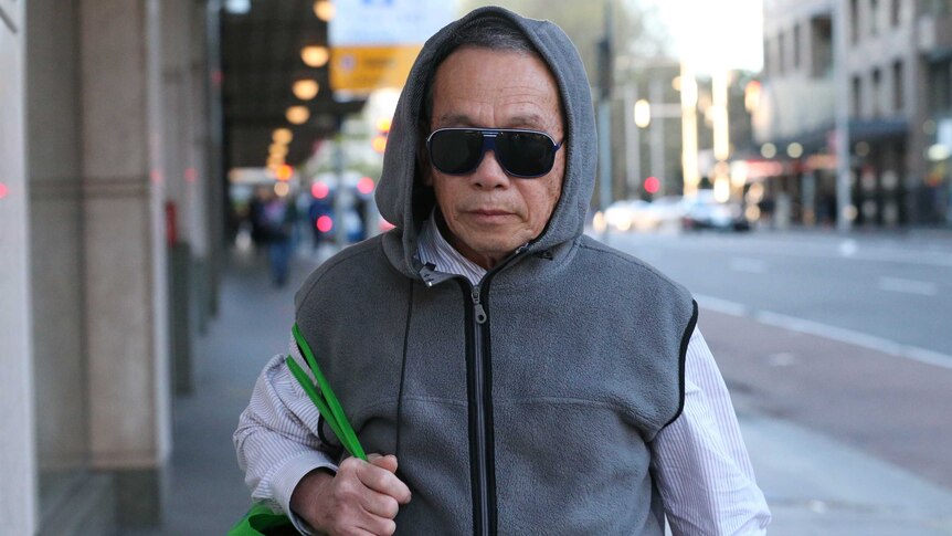 Quy Huy Hoang in sunglasses and a hooded jumper outside court.